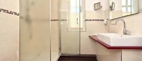 Une salle de bain avec une douche à parois de verre, un lavabo blanc doté d’un plan de toilette rouge, et un miroir au-dessus du lavabo.
