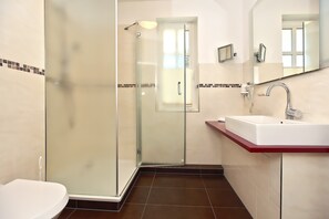 A bathroom with a glass shower enclosure, a white sink with a red countertop, and a mirror above the sink. - The spacious Comfort apartment offers pure relaxation. (Ahrenshoop)