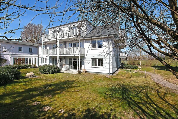 A two-story building with a balcony, a paved pathway, and a grassy lawn. - The spacious Comfort apartment offers pure relaxation. (Ahrenshoop)