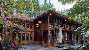 A rustic wooden house with a thatched roof, large windows, and a covered outdoor seating area. - Mat Retreat (Hanoi)