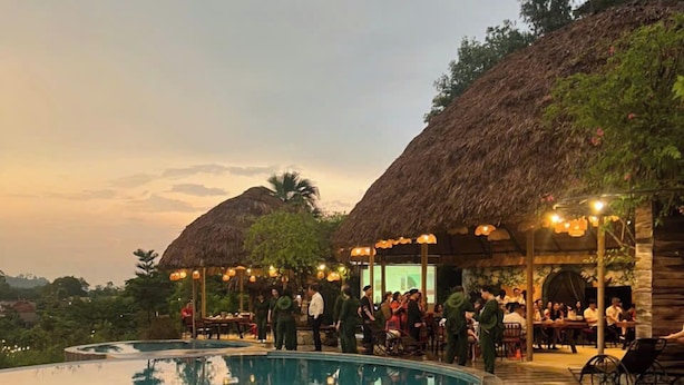 A poolside area with a thatched-roof structure, a bar area, and a group of people gathered around tables. - Mat Retreat (Hanoi)