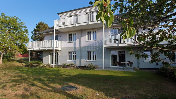 A two-story building with a balcony, a lawn, and a tree in the foreground. - The particularly spacious Apartment Suite offers pure relaxation. (Ahrenshoop)