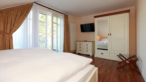 A bedroom with a large bed, a wardrobe, a TV mounted on the wall, and a window with curtains. - The particularly spacious Apartment Suite offers pure relaxation. (Ahrenshoop)