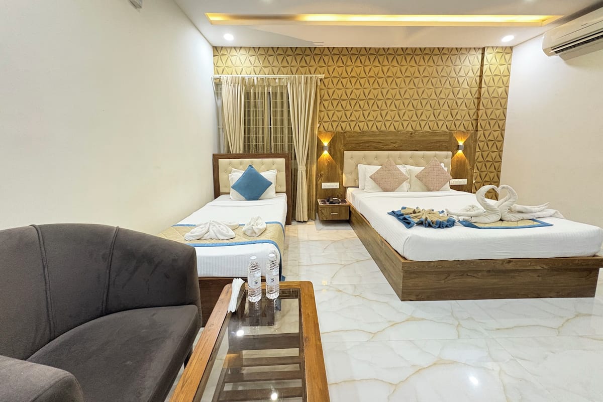 Una habitación de hotel con dos camas, un sofá, una mesa de centro de vidrio y un minibar.