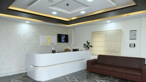 Una zona d'entrada amb una taula de recepció blanca, un sofà marró, un televisor de pantalla plana penjat a la paret i un terra amb un dibuix.