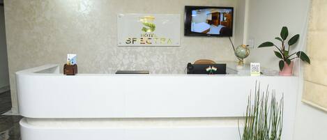 A hotel reception desk with a sign reading "Hotel Spectra," a television mounted on the wall, and a potted plant.