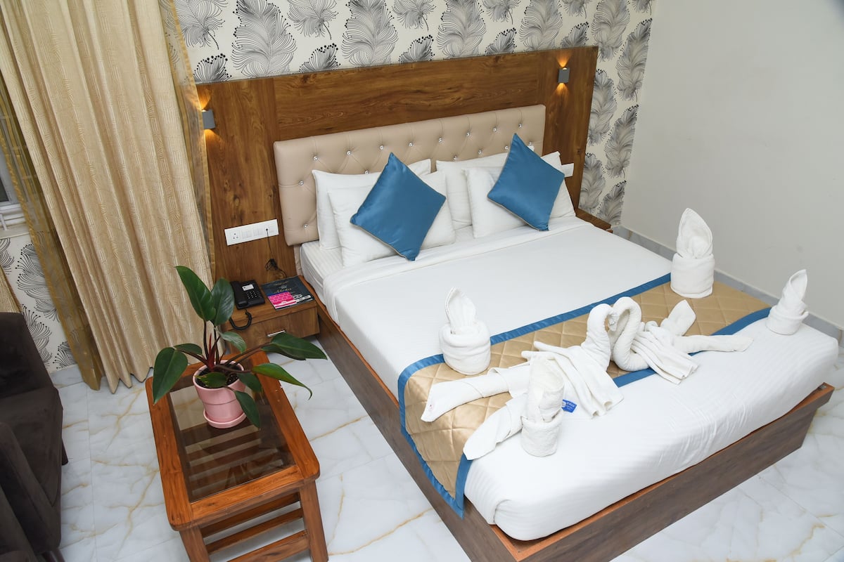 Una habitación de hotel con cama, mesita de noche, planta en maceta y una mesita auxiliar de madera.