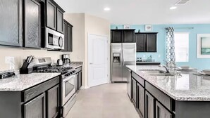 A modern kitchen with dark cabinetry, stainless steel appliances, and a granite countertop. - Solterra Resort!! Spacious House With Game Room, Private Pool and Movie Room!! (Davenport)