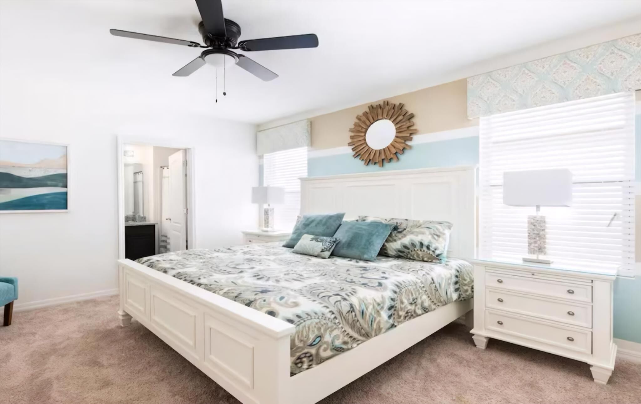 A bedroom with a bed, a nightstand, a dresser, a ceiling fan, and a wall with a decorative mirror.