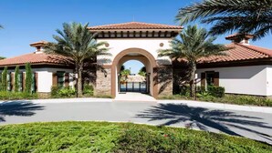 A gated entrance with a central archway, surrounded by palm trees and a well-maintained lawn. - Solterra Resort!! Spacious House With Game Room, Private Pool and Movie Room!! (Davenport)