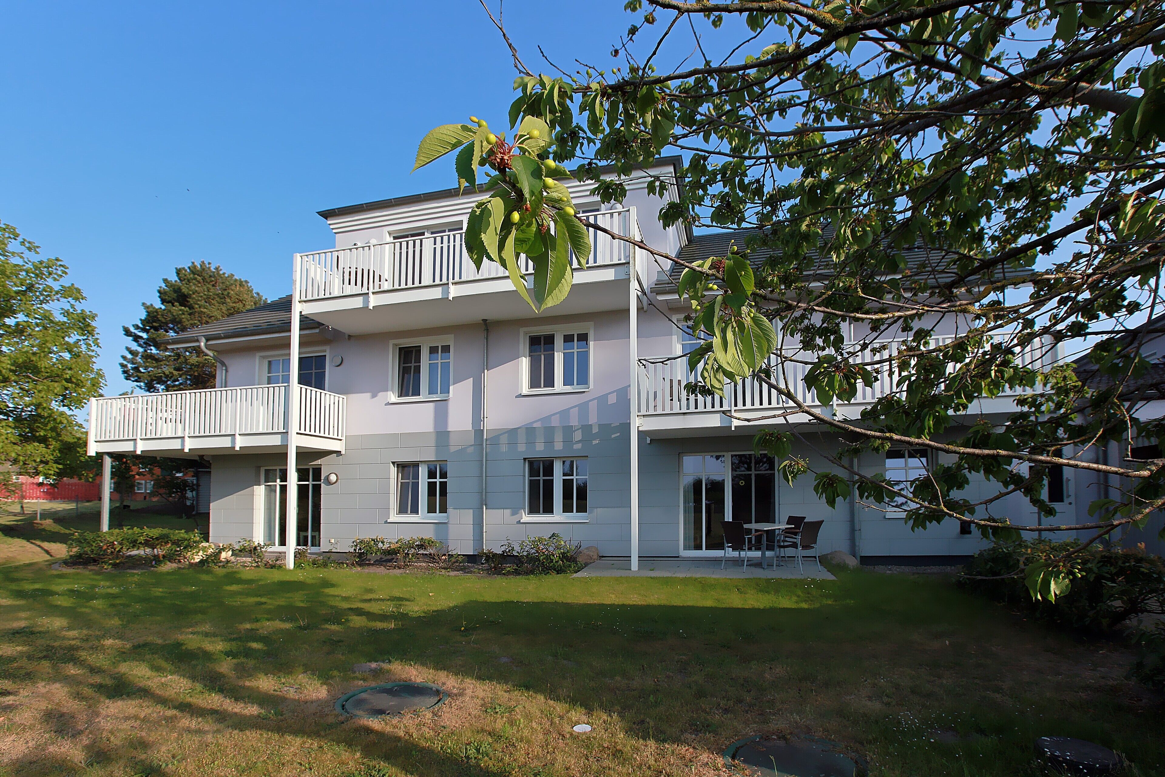 Ein zweigeschossiges Wohngebäude mit einem Balkon im oberen Stockwerk, einer Veranda und einem gepflegten Rasen.