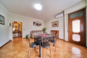 Un espace repas comprenant une table et des chaises, un canapé et une porte dotée d’un panneau en verre dépoli.