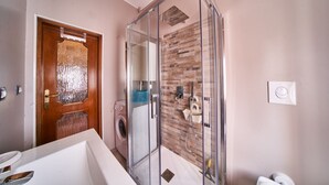 Une salle de bain moderne avec une douche en verre, une porte en bois, un lave-linge et un lavabo blanc.