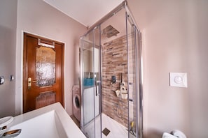 Une salle de bain moderne avec une douche en verre, une porte en bois, un lave-linge et un lavabo blanc.