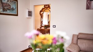 Un salon avec un canapé, un vase de fleurs, un miroir et un tableau accroché au mur.