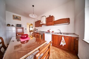 A compact kitchen with wooden cabinets, a built-in microwave, and a dining area with a wooden table and chairs. - Tecla - 3 bedrooms with garage and WiFi (Sirmione)