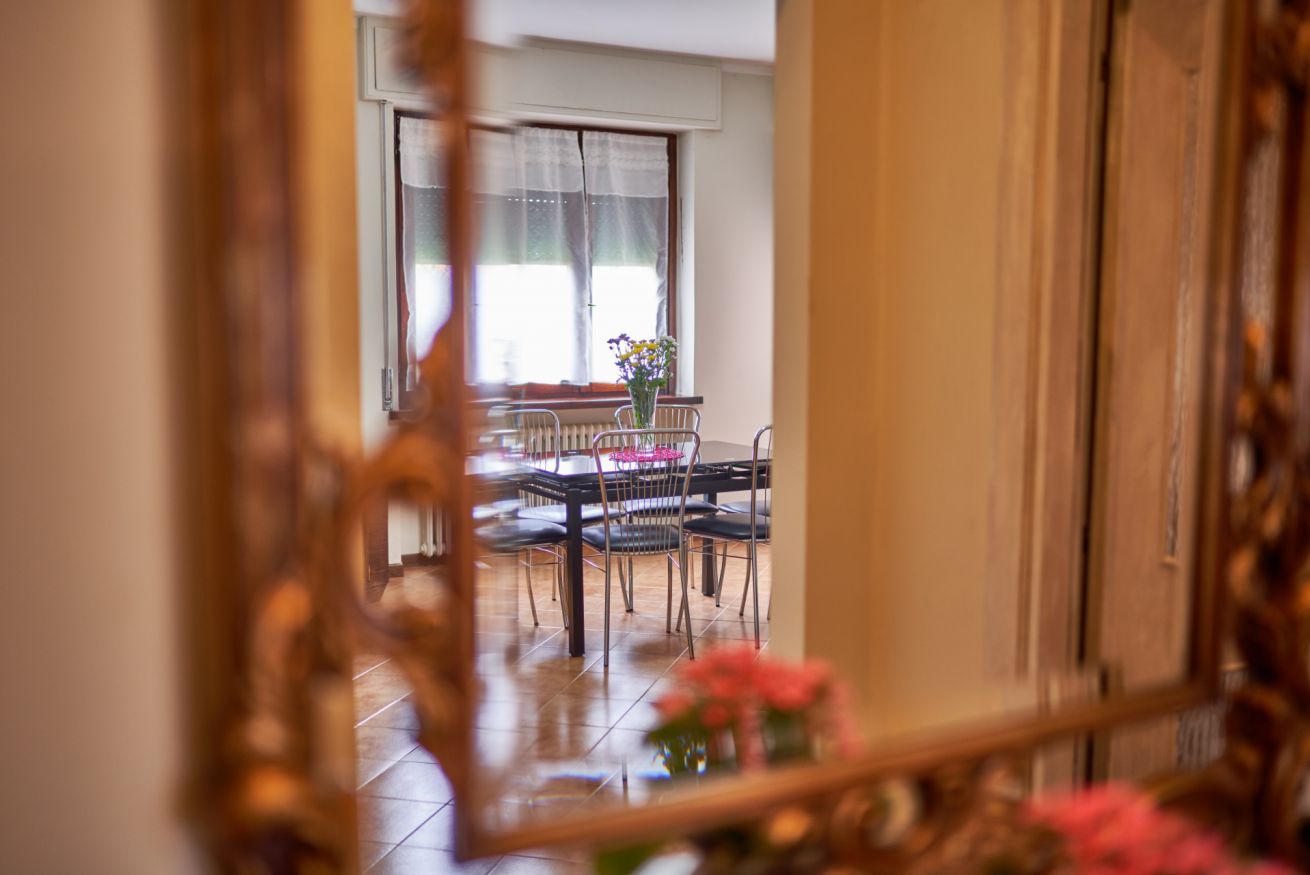 A dining area with a table and chairs, a window with curtains, and a vase with flowers.