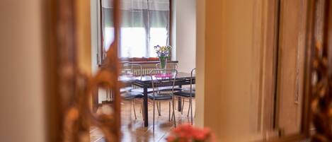 A dining area with a table and chairs, a window with curtains, and a vase with flowers.