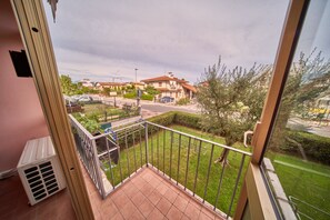 Un balcon donnant sur un quartier résidentiel, une rue et une voiture garée.