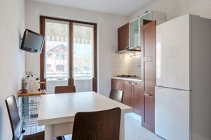 A compact kitchen with a dining table, chairs, a built-in TV, and a refrigerator.