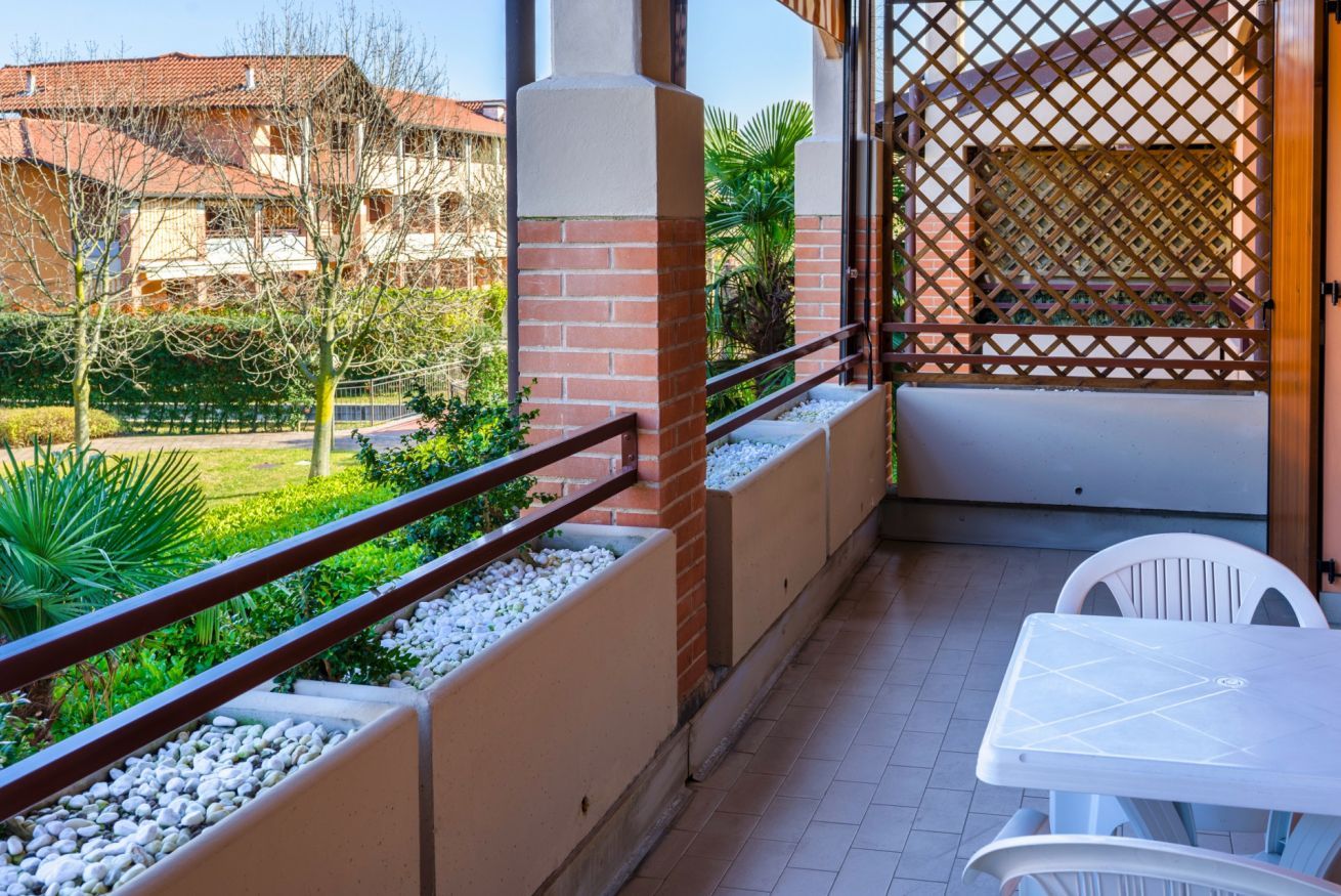 A balcony with a view of a garden, a white table, and a chair.