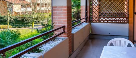 Un balcón con vistas a un jardín, una mesa blanca y una silla.