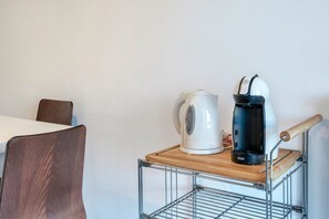 A metal cart with a kettle and a coffee maker on a wooden surface.
