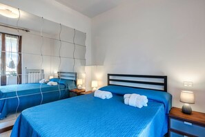 Ein Hotelzimmer mit zwei Betten, jeweils mit blauer Bettwäsche und weißen Handtüchern. An den Betten stehen Nachttischlampen, und an der Wand befindet sich ein Spiegel.