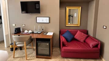 Una habitación compacta con escritorio de madera, sofá rojo, televisor y un refrigerador pequeño.