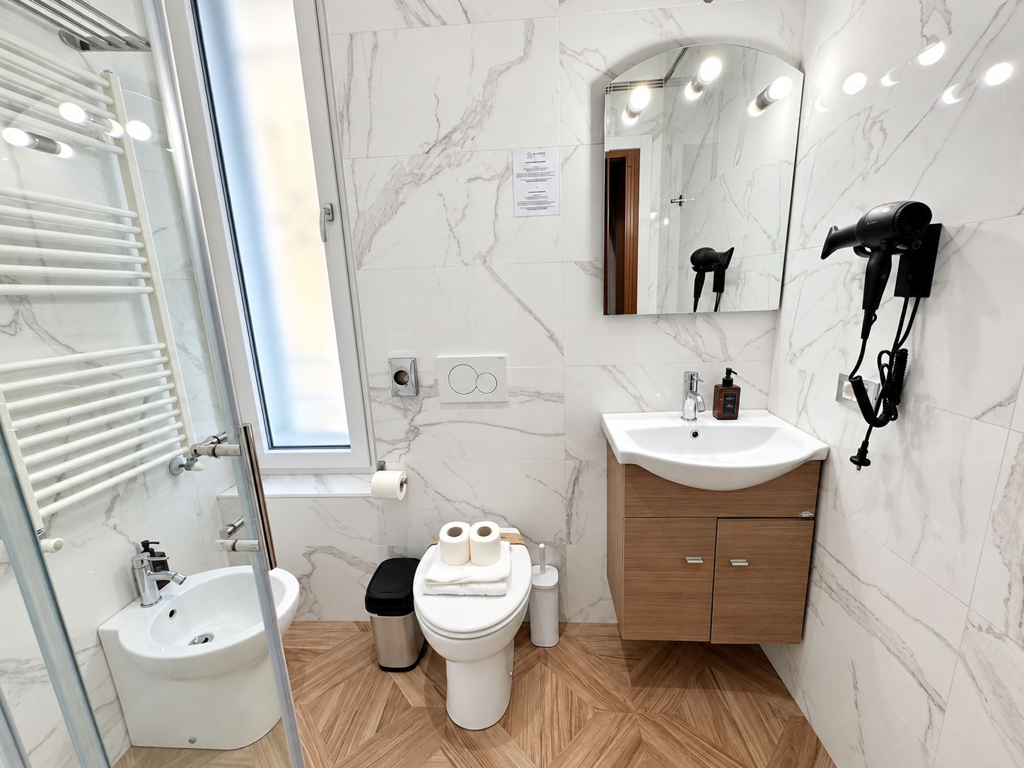 A modern bathroom with a bidet, a sink, a mirror, and a hairdryer mounted on the wall.