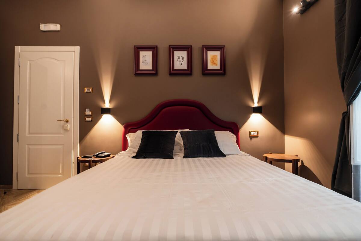 Ein ordentlich gemachtes Bett mit einem roten Kopfteil, zwei Nachttischen und drei gerahmten Bildern an der Wand.