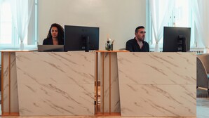 A reception desk with two LG monitors, a vase with a reed diffuser, and a marble-patterned wall. - Whim Collection Vaticano Prati  (Rome)