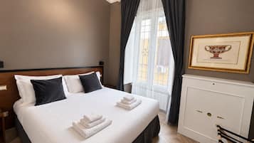 A hotel room with a large bed, a bedside table, a radiator, a chair, and a window with curtains.