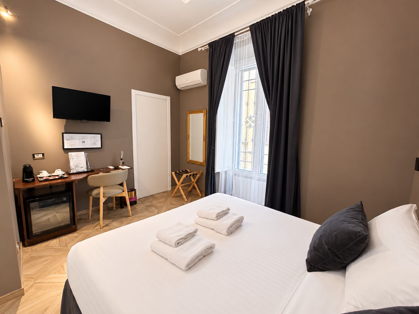 A hotel room with a bed, a desk with a chair, a television, and a window with curtains.