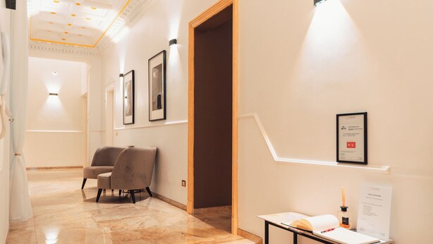 Un hall d’hôtel avec un sol en marbre, un comptoir d’accueil, des œuvres d’art encadrées accrochées aux murs et un escalier menant à un autre espace.