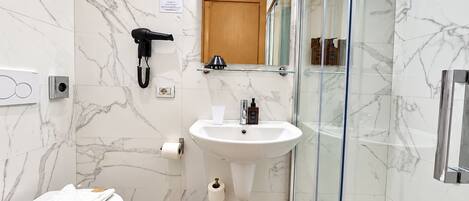 A modern bathroom with a marble floor, a white sink, a glass shower enclosure, a toilet, and a hairdryer.