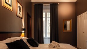 Une chambre d’hôtel avec un lit bien fait, une lampe de chevet, une fenêtre avec des rideaux et un miroir encadré accroché au mur.