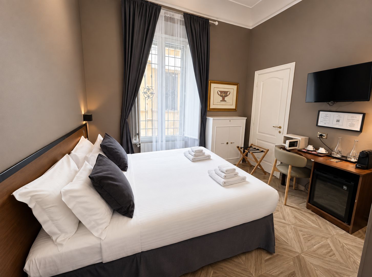 Habitació d'hotel amb un llit, escriptori amb ordinador, televisió i finestra amb cortines.