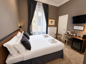 A hotel room with a bed, a desk with a computer, a television, and a window with curtains. - Whim Collection Vaticano Prati  (Rome)