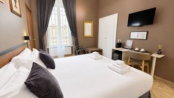 A hotel room with a large bed, a desk, a chair, a television, and a window with curtains.