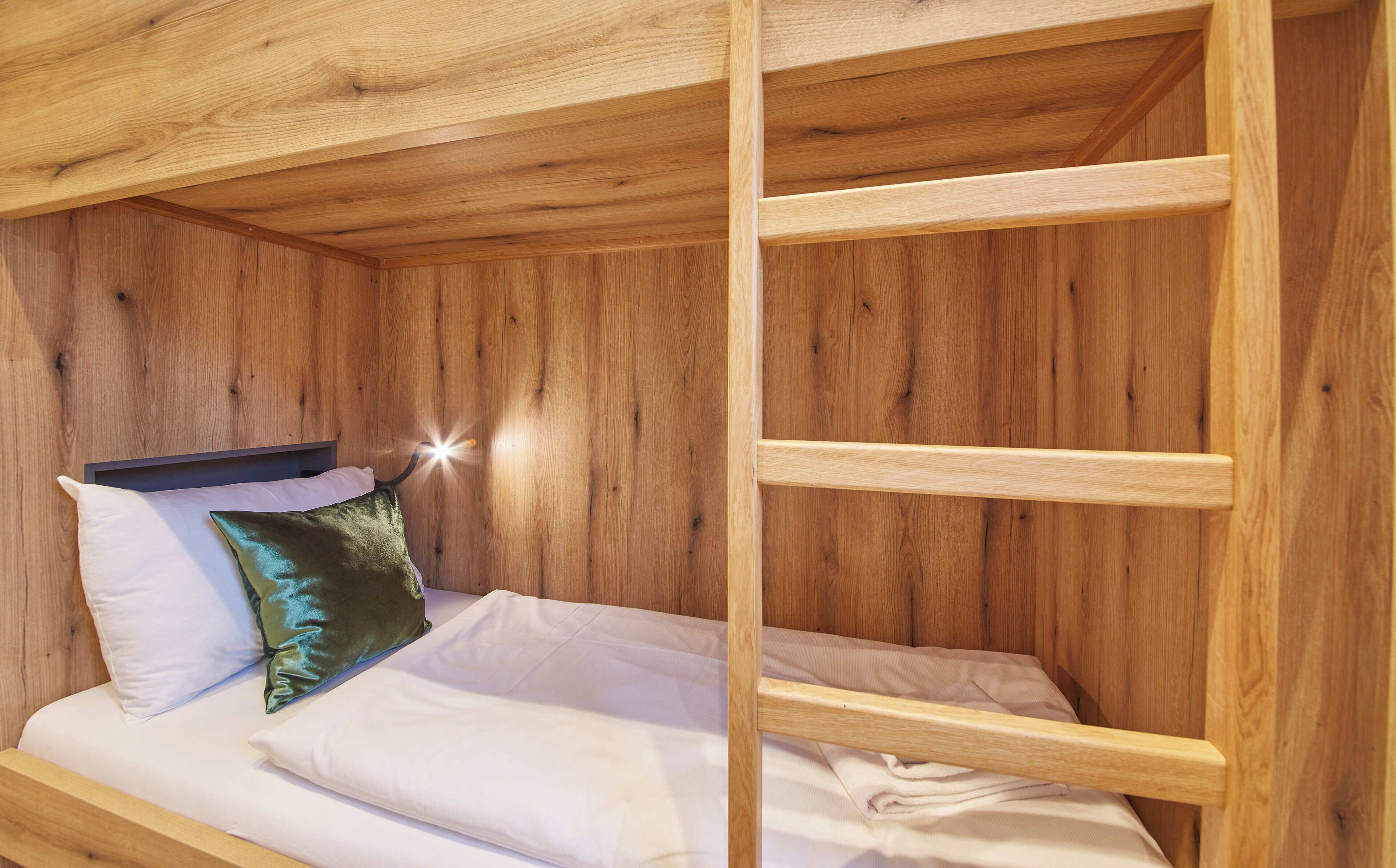A wooden bunk bed with white bedding and a green pillow.