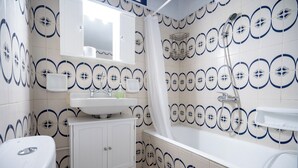 Une salle de bain équipée de toilettes, d’un lavabo, d’un meuble de rangement et d’une baignoire avec pommeau de douche.