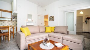 Un salon avec un canapé beige, des coussins jaunes, une table basse en bois et un coin repas comprenant des chaises et une table en bois.