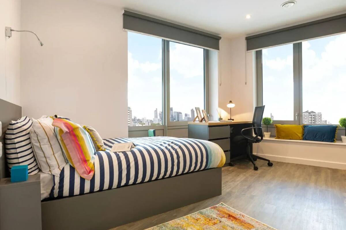 A modern bedroom with a large bed, a desk, and a view of the city.