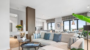 A modern living room with a sofa, coffee table, and a dining area with a table set for four. - Penthouse Suite with Sea View, Balcony, and Fireplace (List auf Sylt)