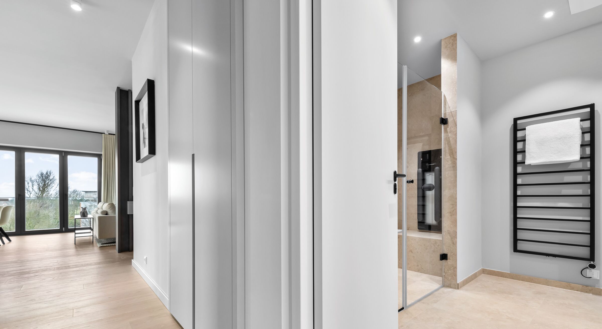 Ein modernes Interieur mit einer großen Schiebetür, die auf einen Balkon führt, ein minimalistisches Badezimmer mit Handtuchhalter und ein heller, freundlicher Boden.