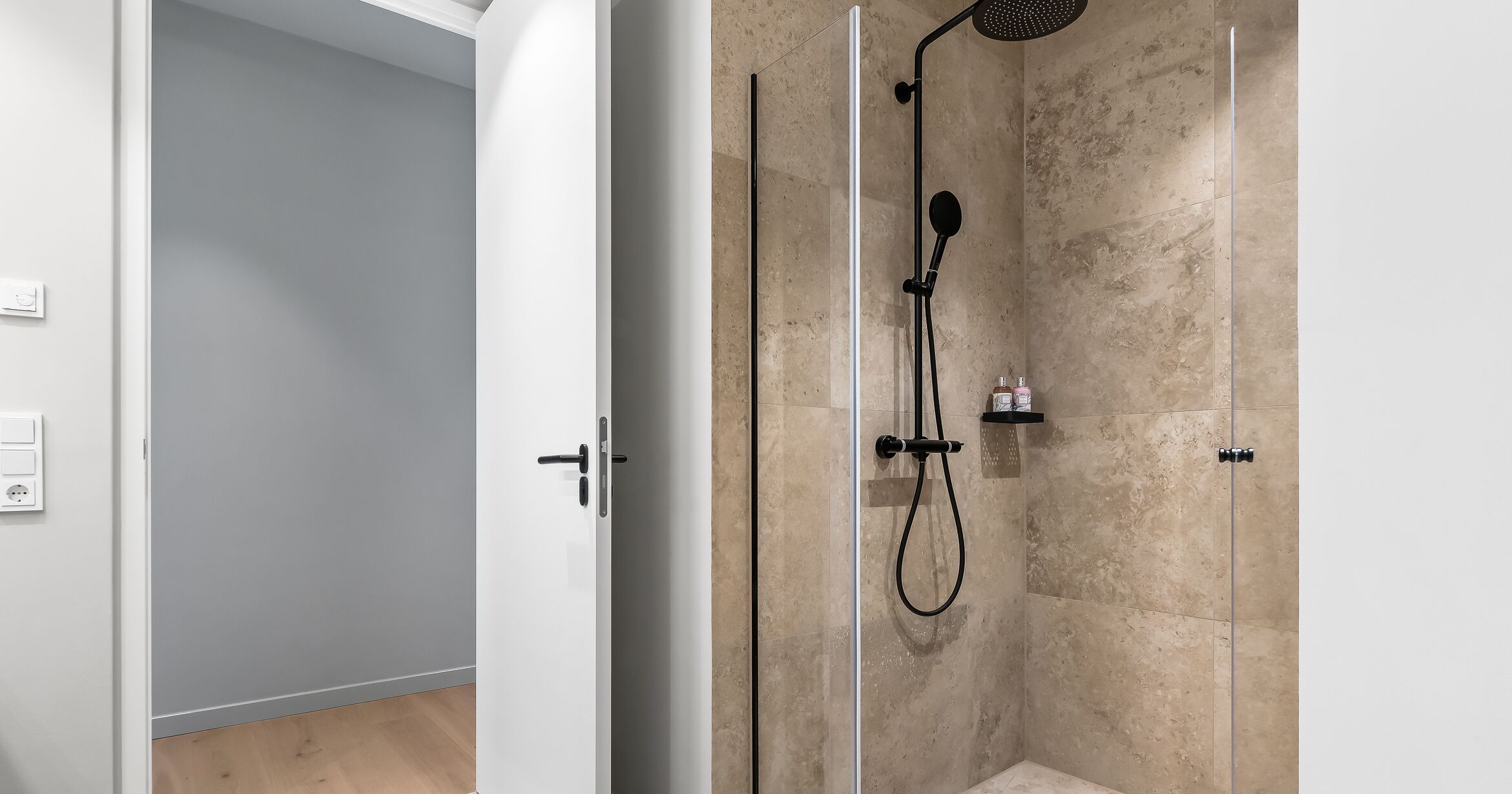 Une salle de bain moderne avec une douche à l’italienne en verre, des carreaux de couleur beige et une porte blanche.