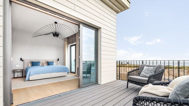 A bedroom with a large bed, a ceiling fan, and a sliding glass door leading to a balcony with wicker furniture. - Penthouse Suite with Sea View, Balcony, and Fireplace (List auf Sylt)