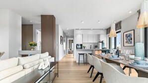 A modern kitchen with white cabinets, a dining area with a wooden table, and a living room with a sofa and a TV. - Penthouse Suite with Sea View, Balcony, and Fireplace (List auf Sylt)