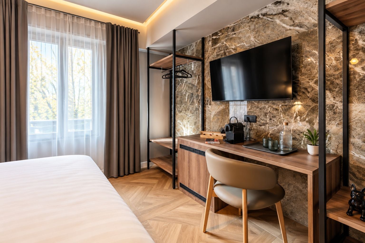 A hotel room with a bed, a desk with a chair, a television, and a stone wall.